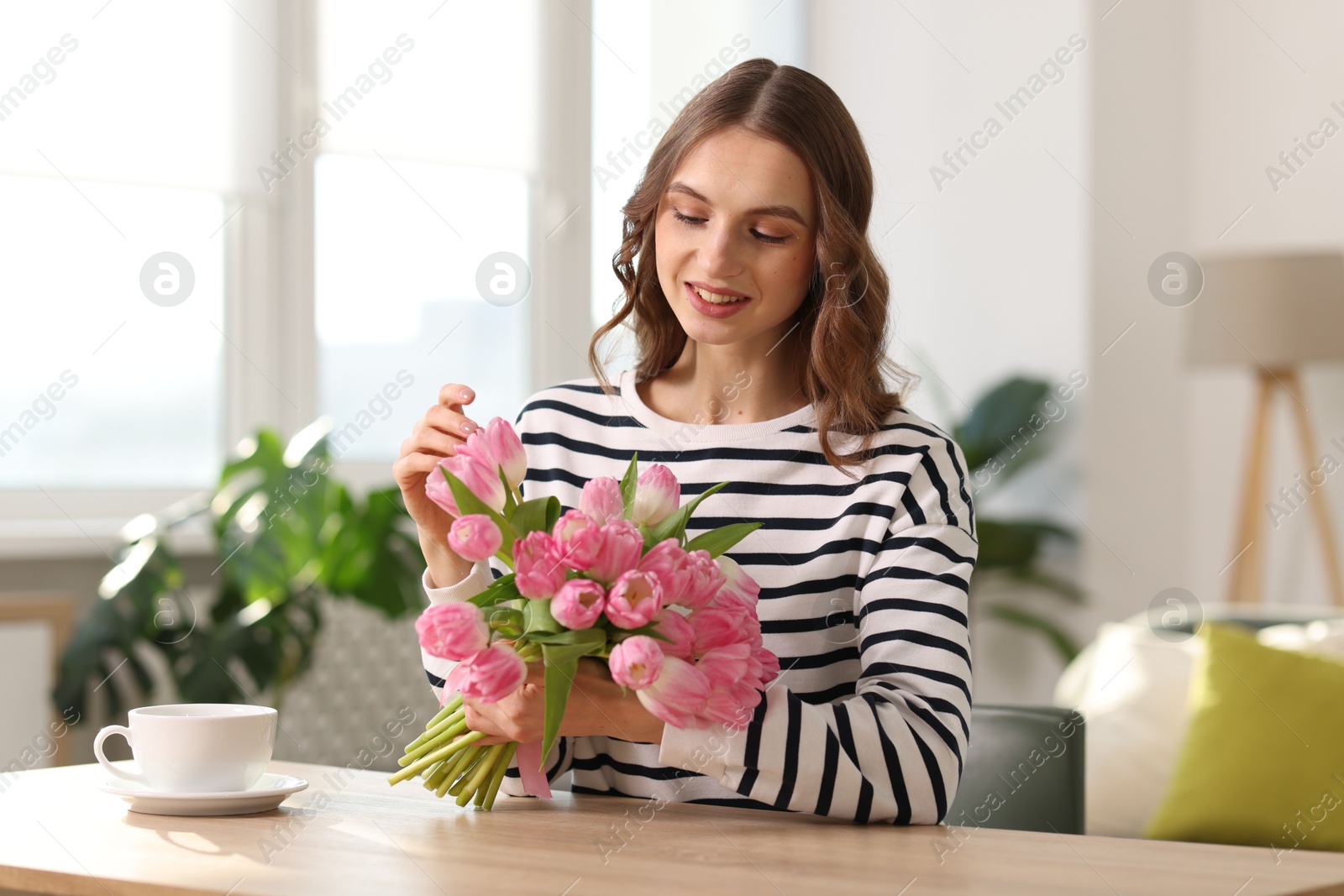 Photo of Smiling woman with bouquet of tulips at table indoors