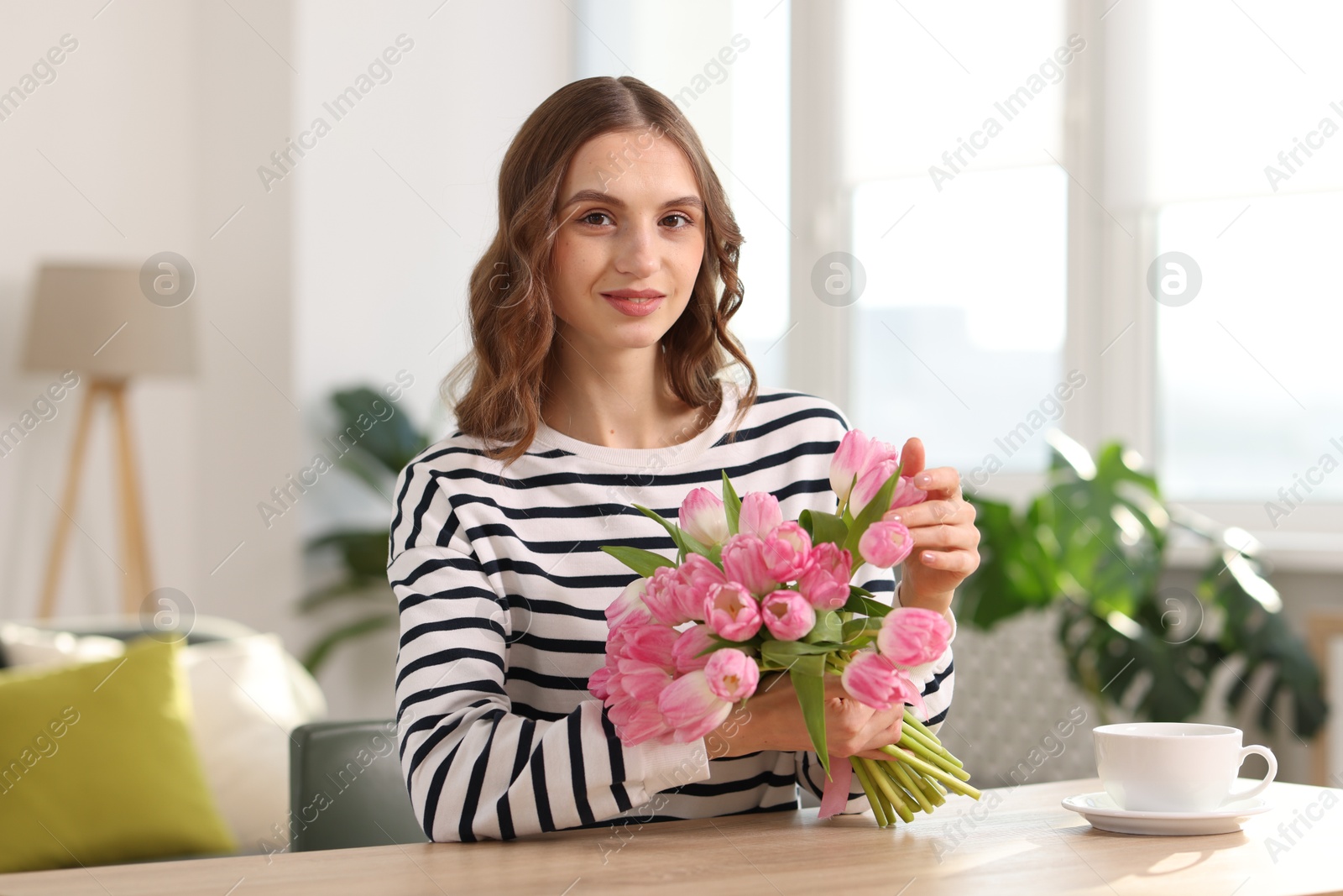 Photo of Beautiful woman with bouquet of tulips at table indoors