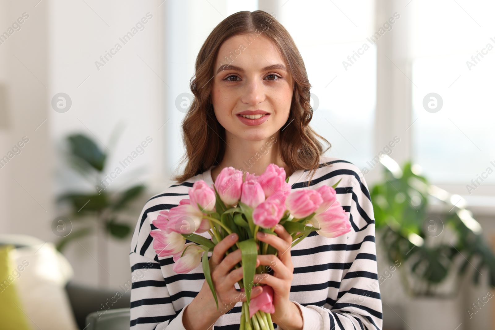 Photo of Smiling woman with bouquet of tulips at home