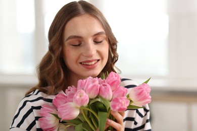 Photo of Smiling woman with bouquet of tulips at home