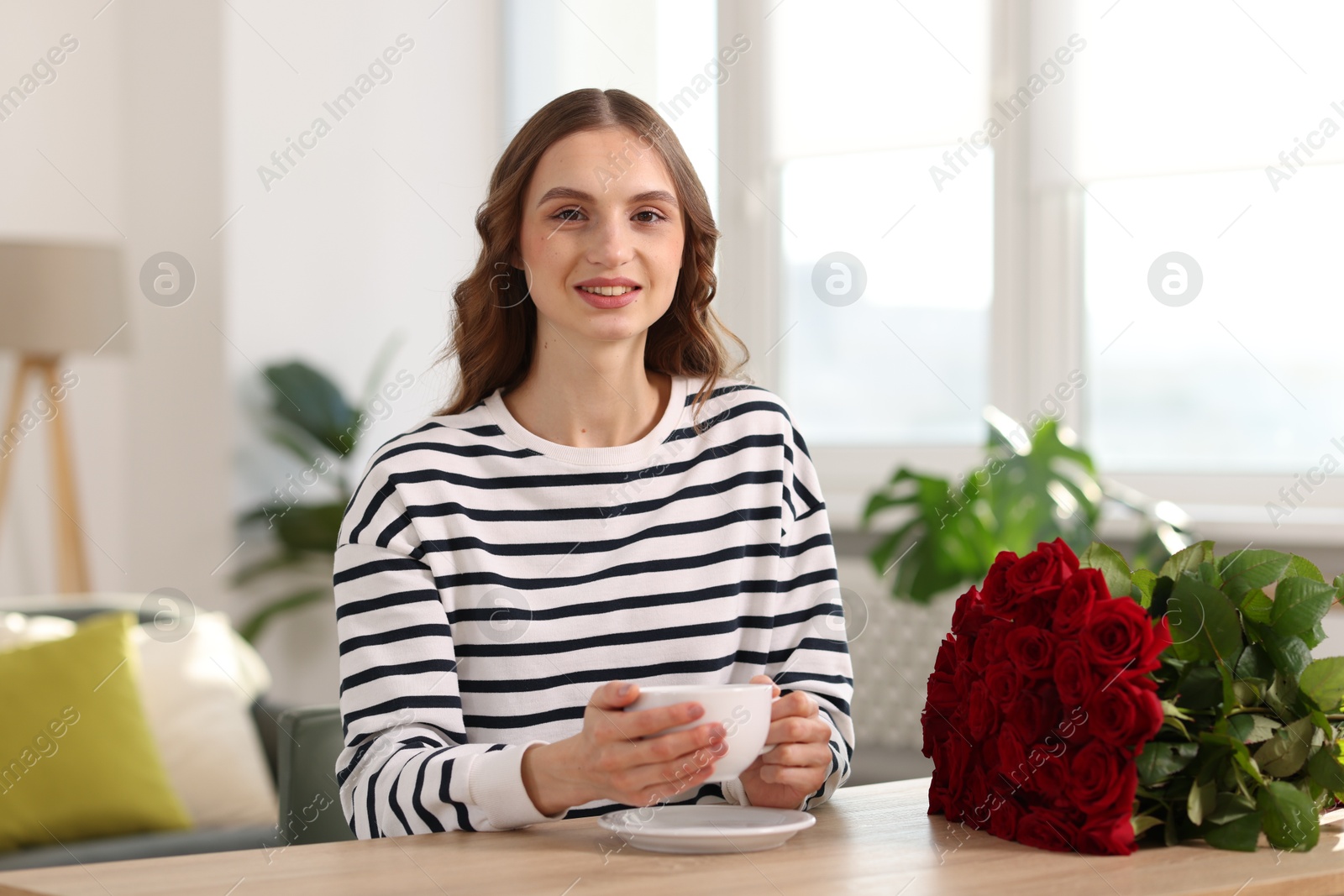 Photo of Smiling woman with bouquet of roses at table indoors