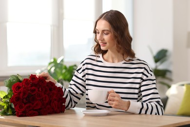 Photo of Smiling woman with bouquet of roses at table indoors