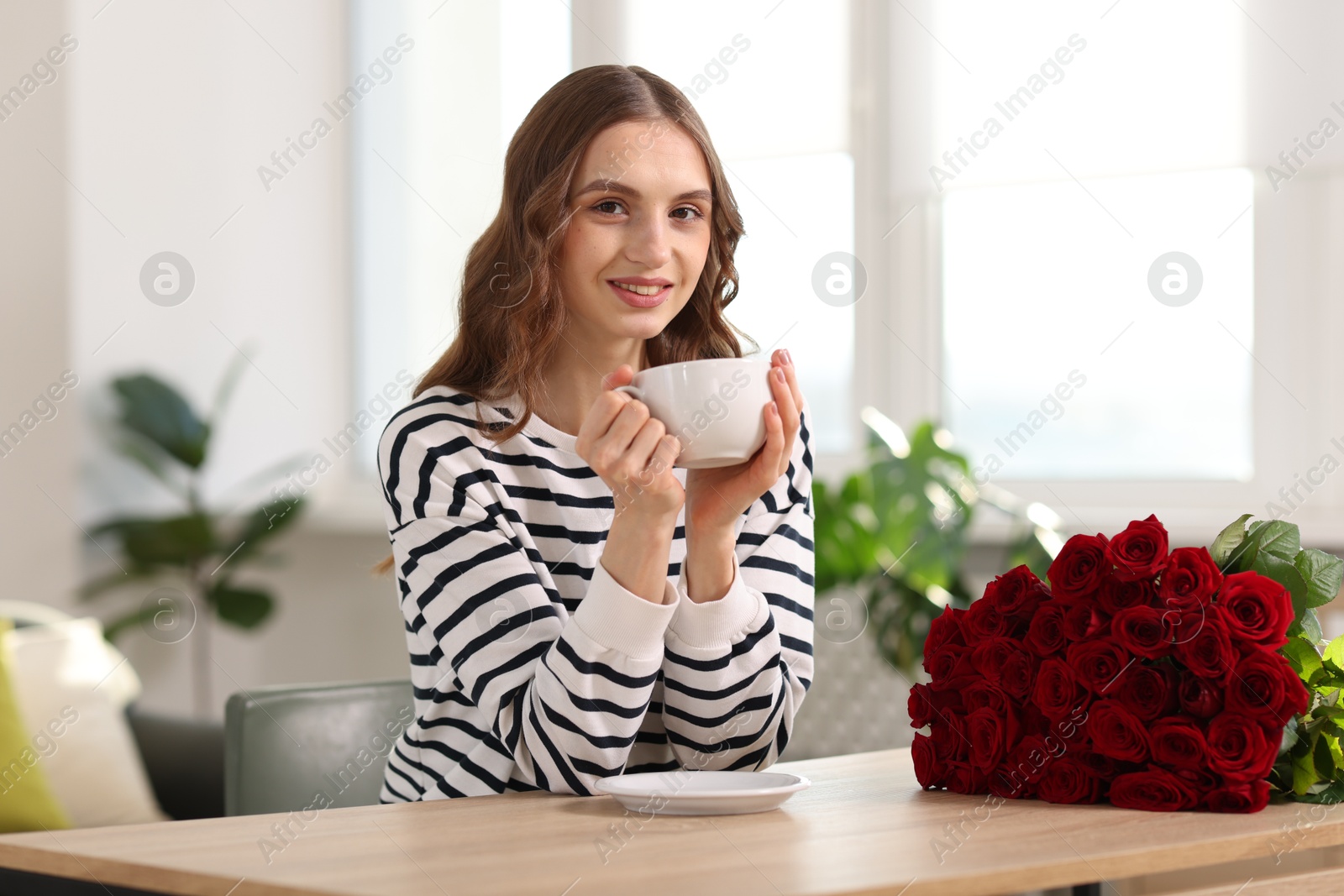 Photo of Smiling woman with bouquet of roses at table indoors