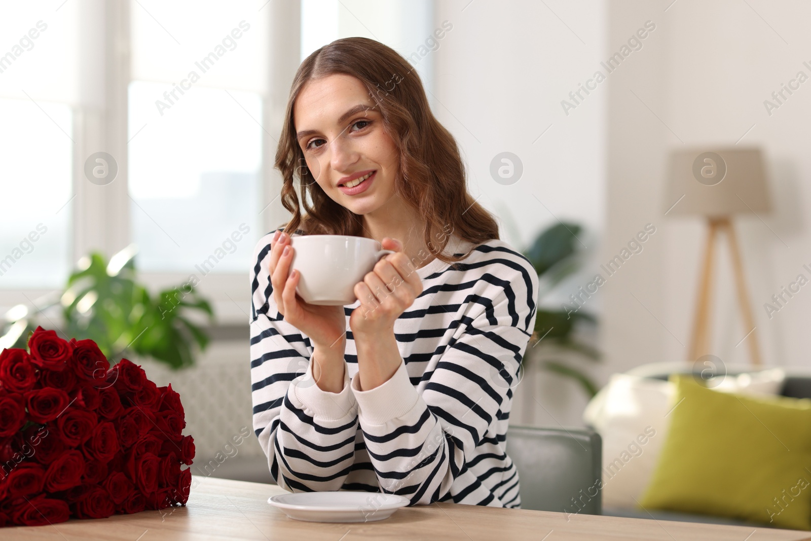 Photo of Smiling woman with bouquet of roses at table indoors