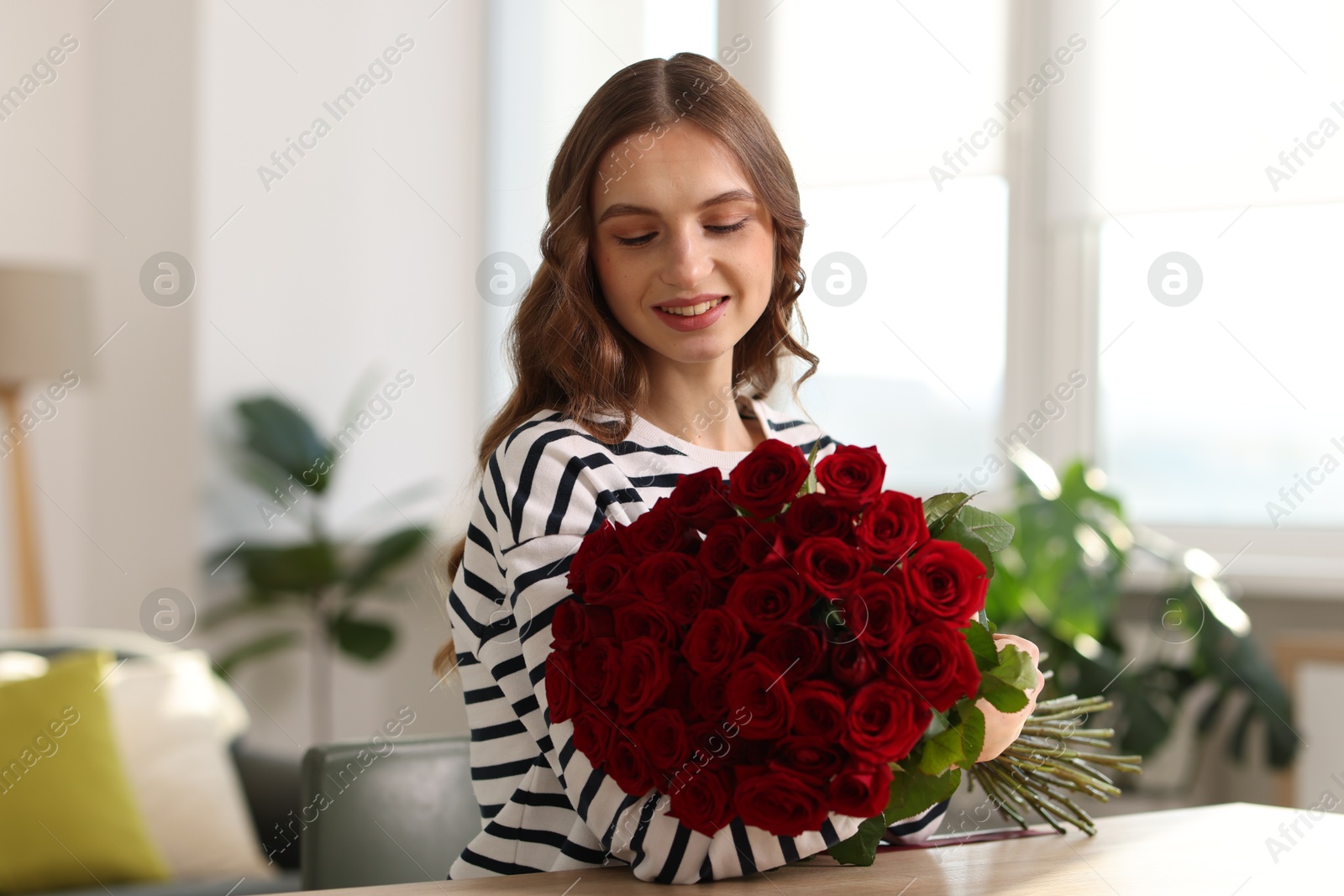 Photo of Smiling woman with bouquet of roses at table indoors