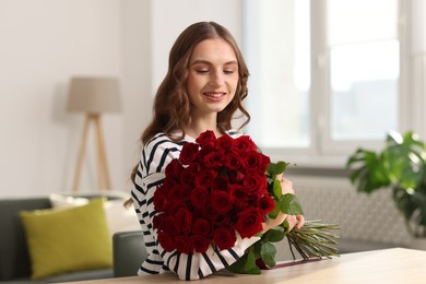 Photo of Smiling woman with bouquet of roses at table indoors