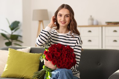 Photo of Smiling woman with bouquet of roses on sofa at home