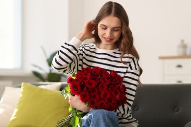 Photo of Smiling woman with bouquet of roses on sofa at home