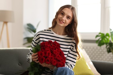 Photo of Smiling woman with bouquet of roses on sofa at home