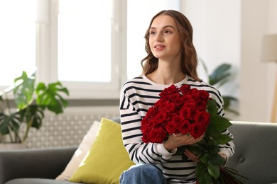 Photo of Smiling woman with bouquet of roses on sofa at home