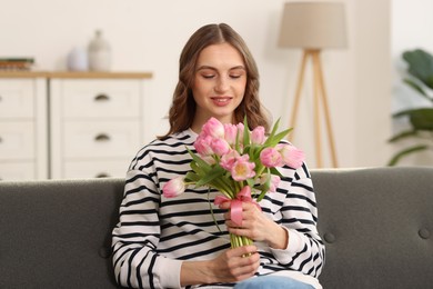 Photo of Smiling woman with bouquet of tulips on sofa at home