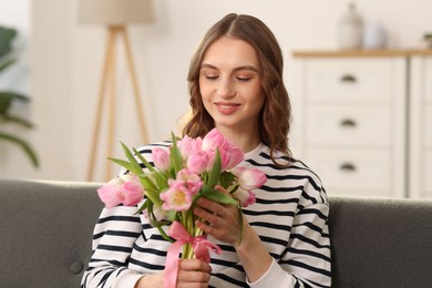 Photo of Smiling woman with bouquet of tulips on sofa at home