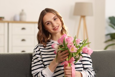 Photo of Smiling woman with bouquet of tulips on sofa at home