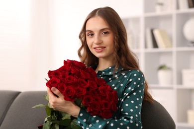 Photo of Smiling woman with bouquet of roses on sofa at home