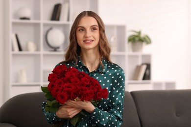 Photo of Smiling woman with bouquet of roses on sofa at home