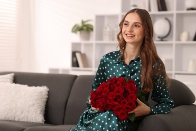 Photo of Smiling woman with bouquet of roses on sofa at home. Space for text