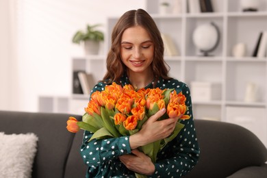 Photo of Smiling woman with bouquet of tulips on sofa at home