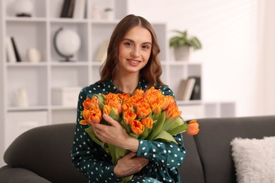 Photo of Smiling woman with bouquet of tulips on sofa at home