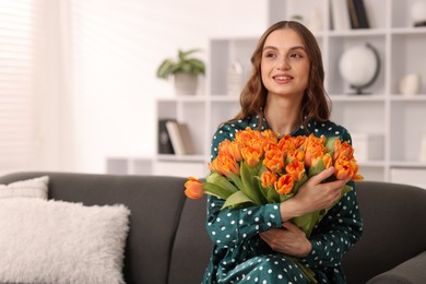 Photo of Smiling woman with bouquet of tulips on sofa at home. Space for text