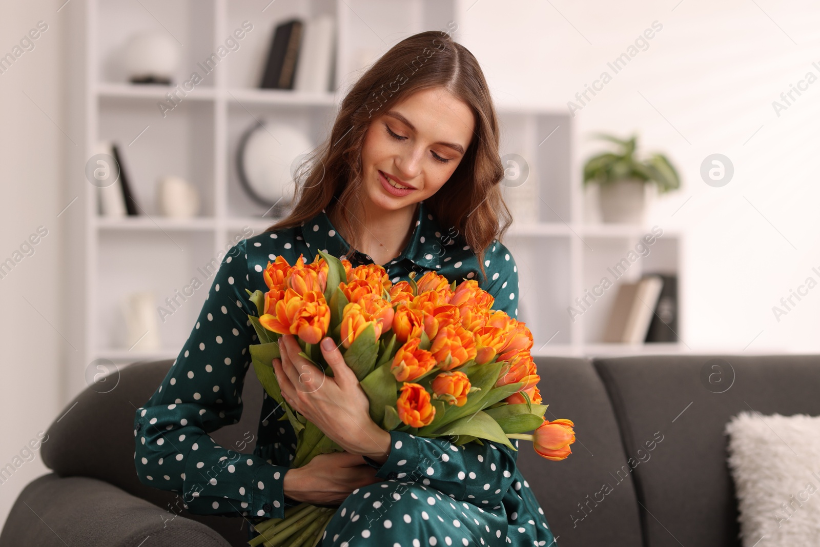 Photo of Smiling woman with bouquet of tulips on sofa at home