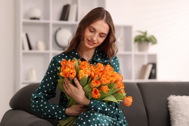 Photo of Smiling woman with bouquet of tulips on sofa at home