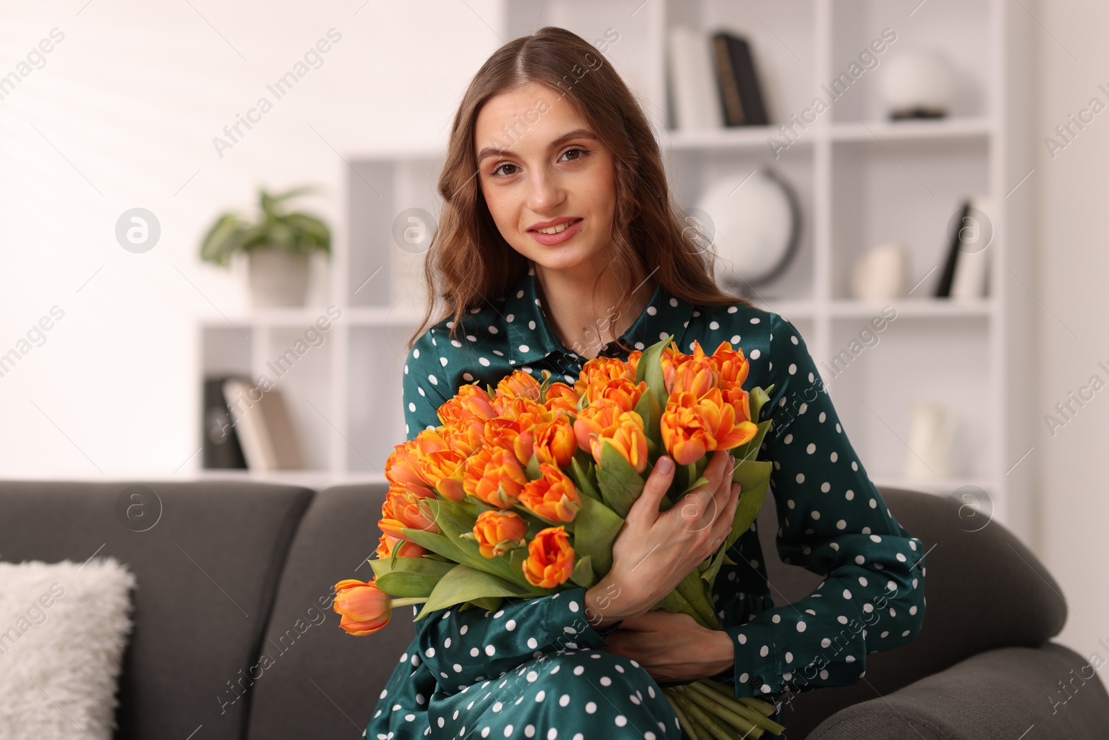 Photo of Smiling woman with bouquet of tulips on sofa at home