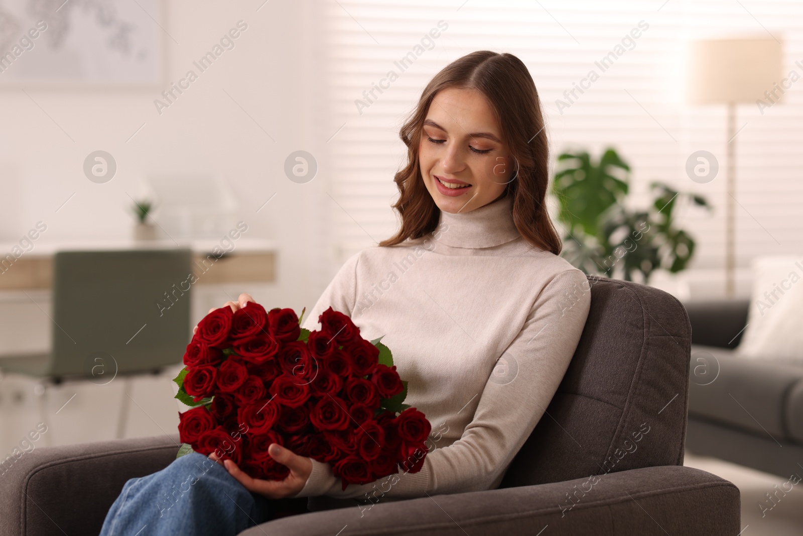 Photo of Smiling woman with bouquet of roses on armchair at home