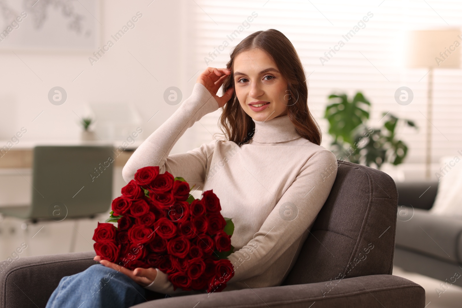 Photo of Smiling woman with bouquet of roses on armchair at home