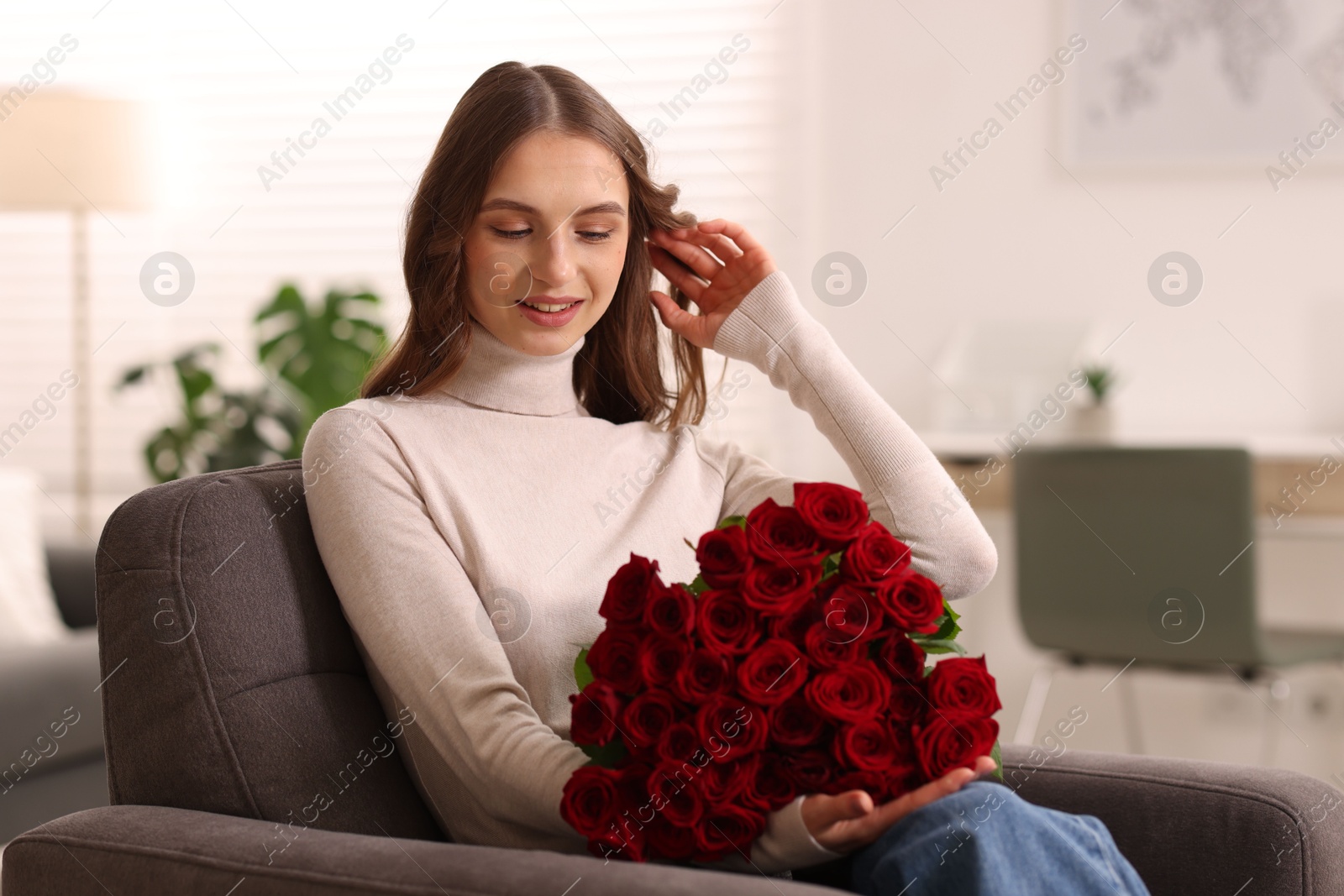 Photo of Smiling woman with bouquet of roses on armchair at home