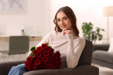 Photo of Smiling woman with bouquet of roses on armchair at home