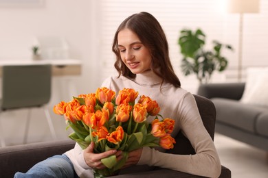 Photo of Smiling woman with bouquet of tulips on armchair at home