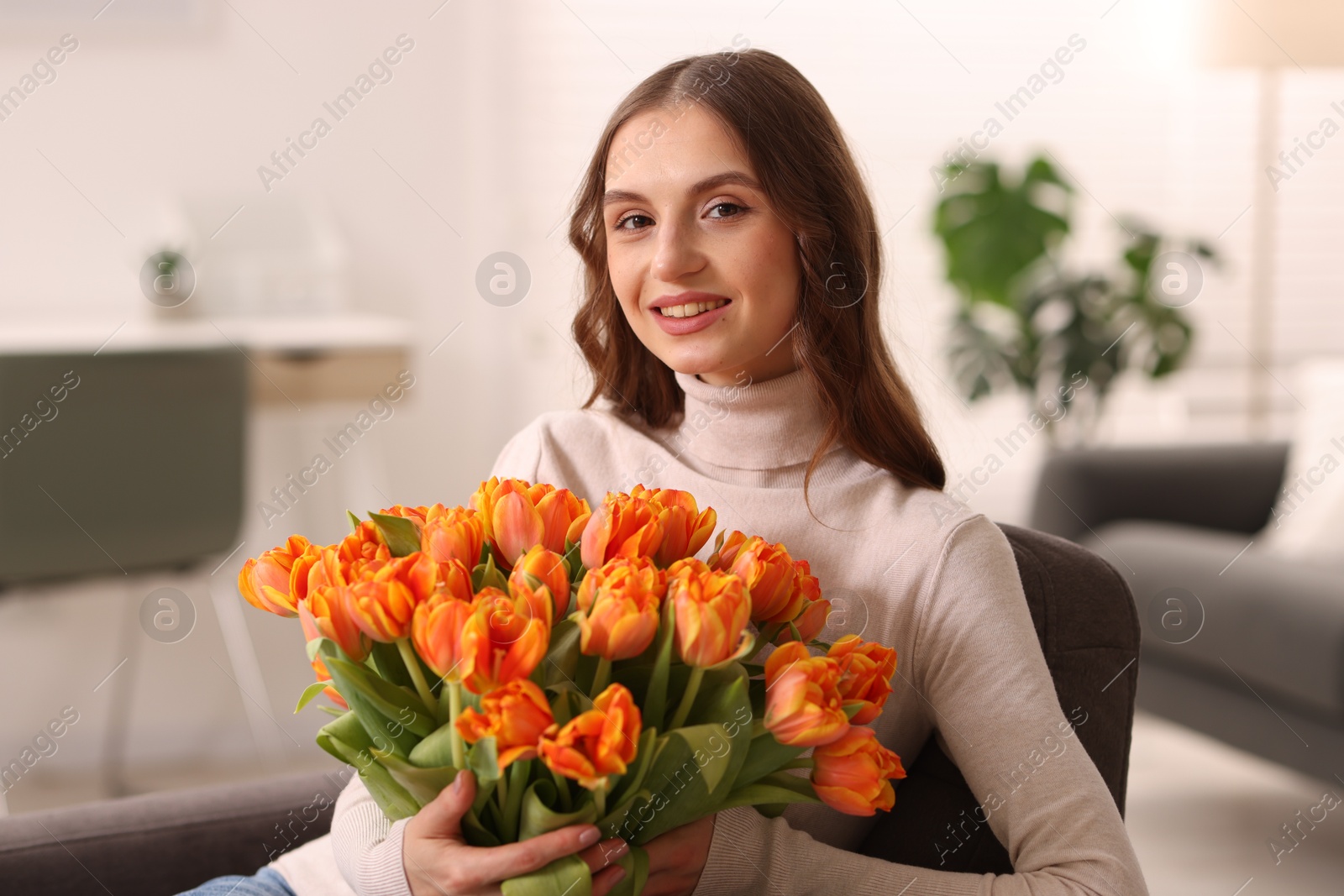 Photo of Smiling woman with bouquet of tulips on armchair at home