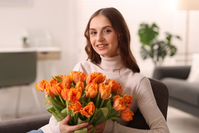 Photo of Smiling woman with bouquet of tulips on armchair at home