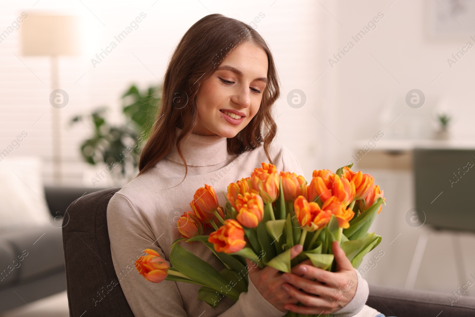 Photo of Smiling woman with bouquet of tulips on armchair at home