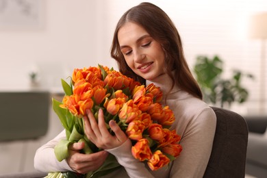 Photo of Smiling woman with bouquet of tulips on armchair at home