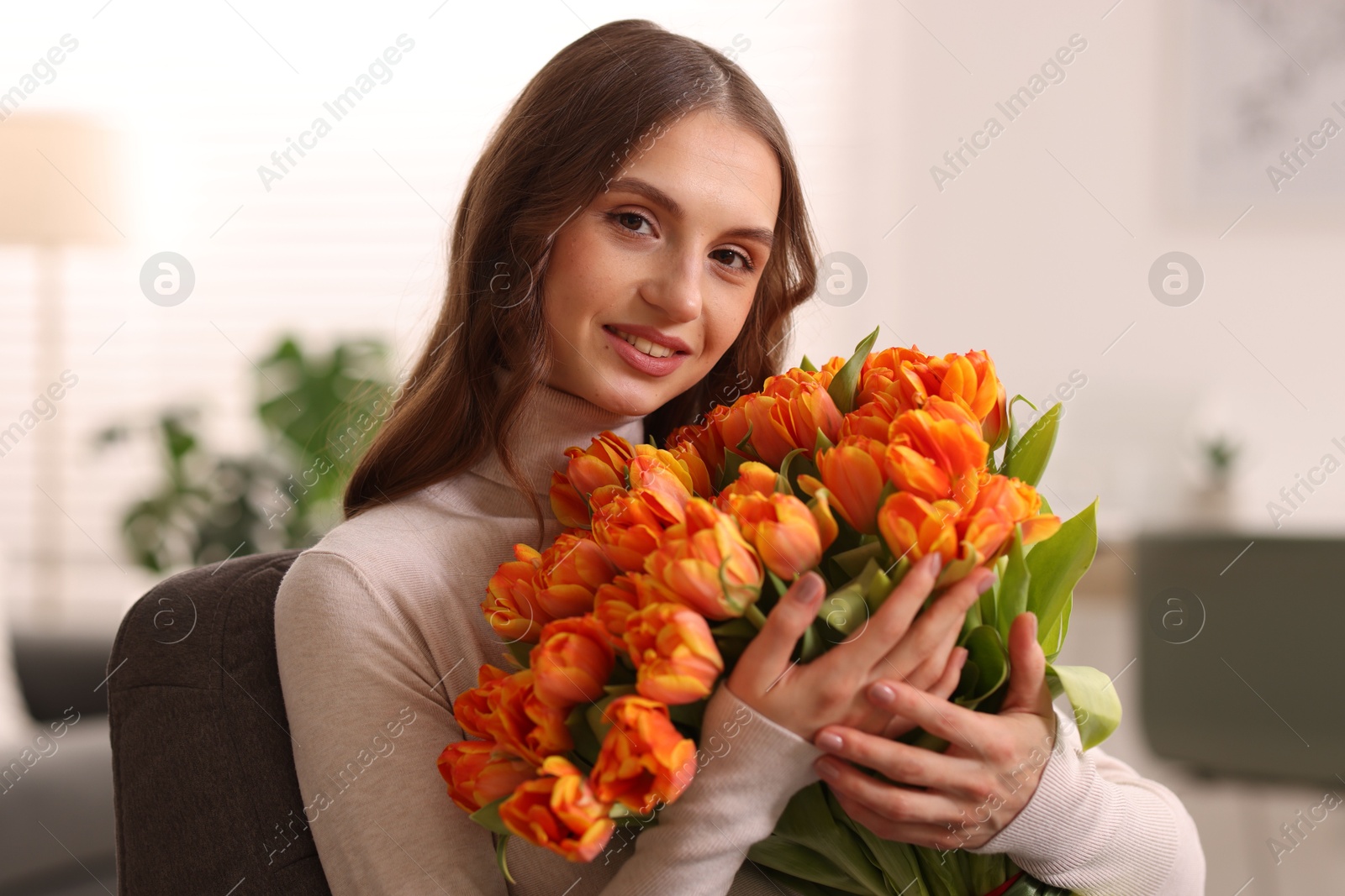 Photo of Smiling woman with bouquet of tulips on armchair at home