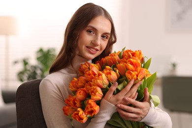 Photo of Smiling woman with bouquet of tulips on armchair at home