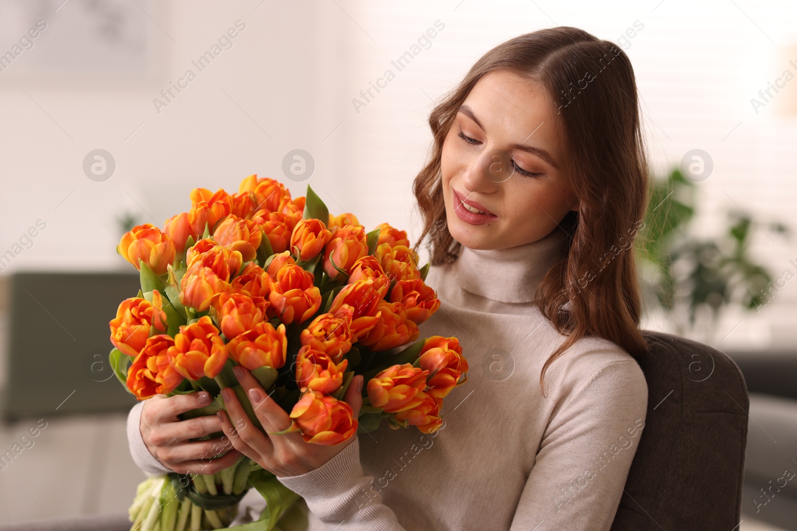 Photo of Smiling woman with bouquet of tulips on armchair at home