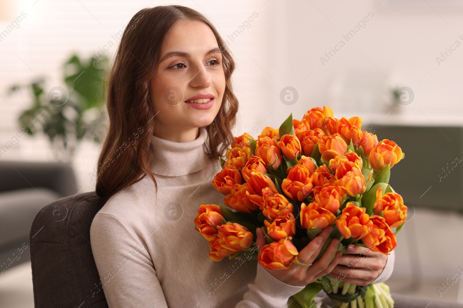 Photo of Smiling woman with bouquet of tulips on armchair at home