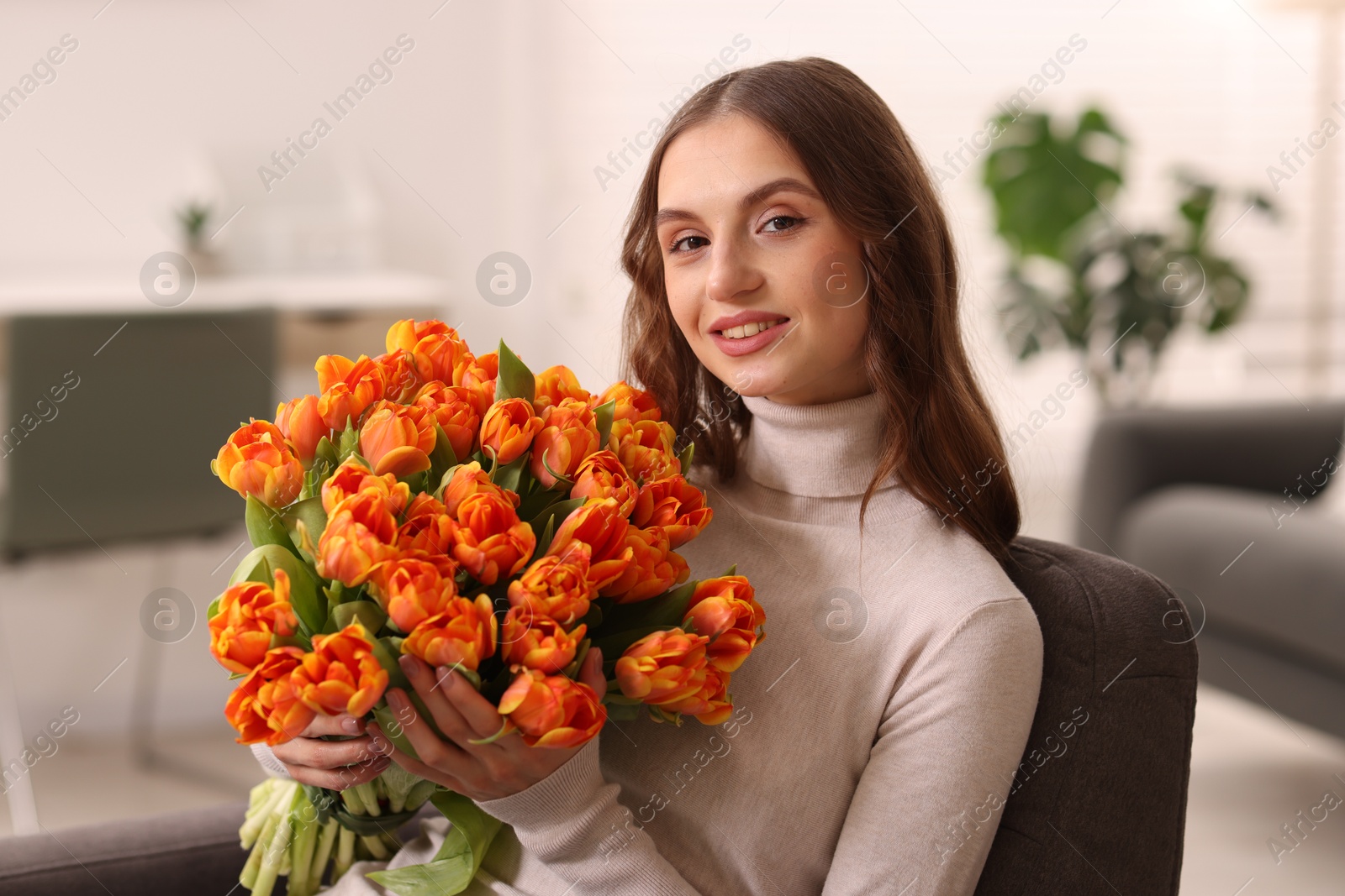 Photo of Smiling woman with bouquet of tulips on armchair at home