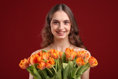 Photo of Smiling woman with bouquet of tulips on dark red background