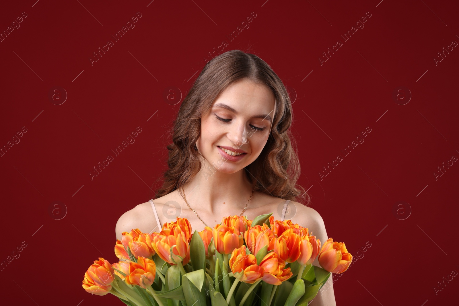 Photo of Smiling woman with bouquet of tulips on dark red background