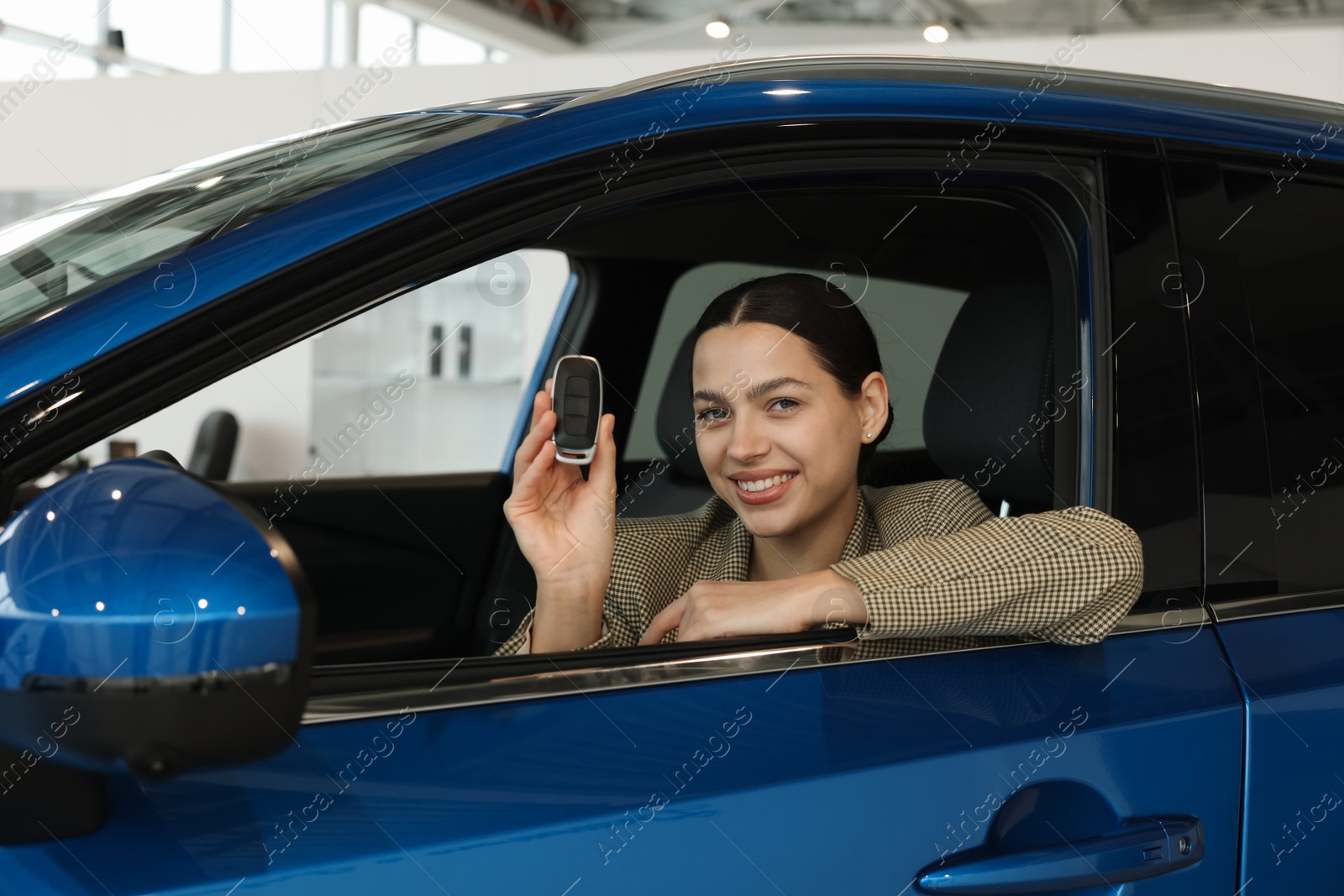 Photo of Happy woman with key inside new car in salon