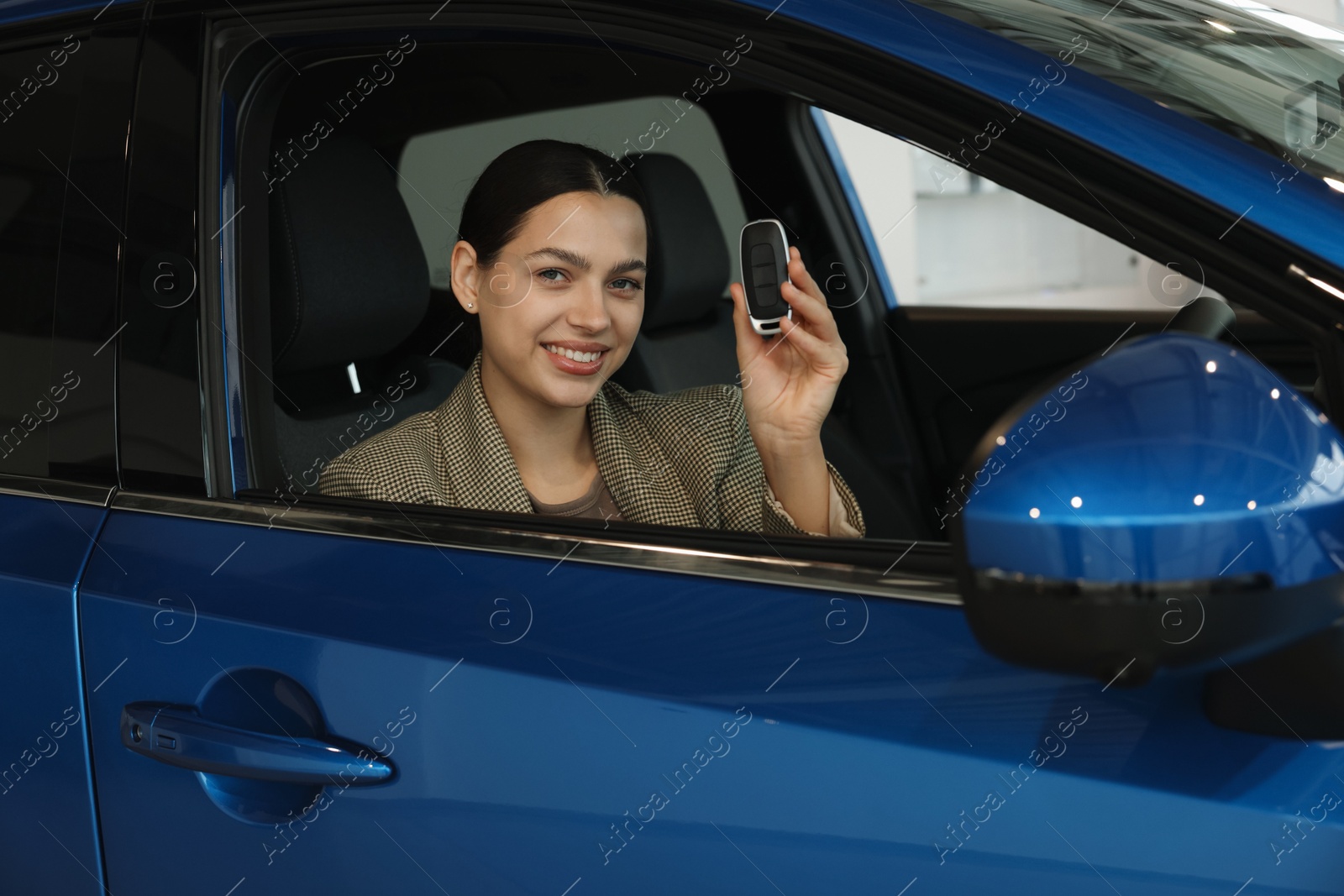 Photo of Happy woman with key inside new car in salon