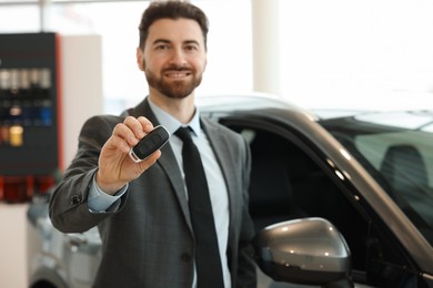 Photo of Happy salesman with key near new car in salon, selective focus