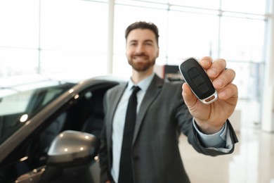 Photo of Happy salesman with key near new car in salon, selective focus