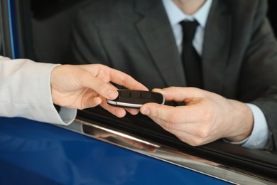 Photo of Saleswoman giving key to client inside new car in salon, closeup