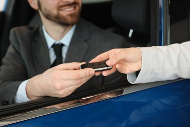 Photo of Saleswoman giving key to client inside new car in salon, closeup