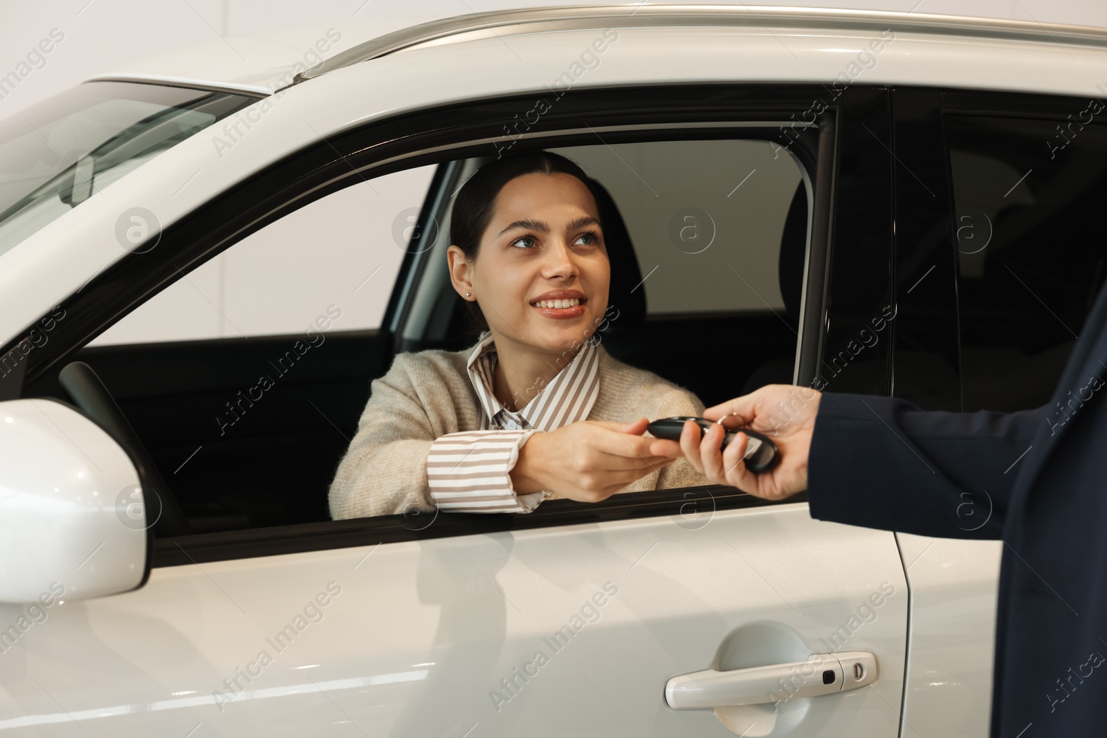 Photo of Salesman giving key to happy client inside new car in salon