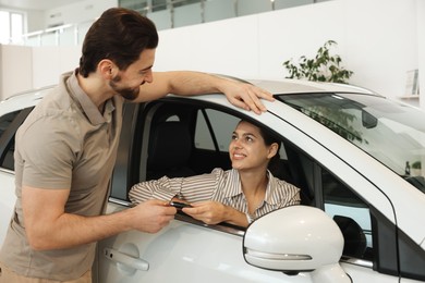 Photo of Happy husband giving key to his wife inside new car in salon